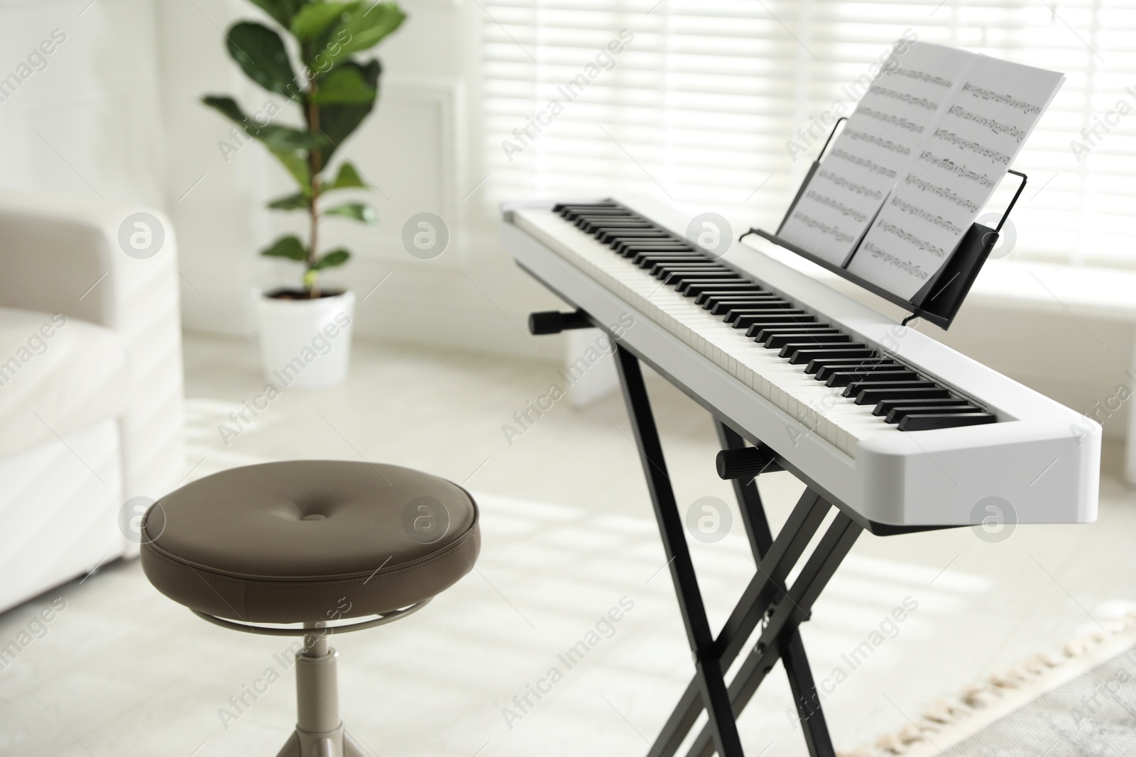 Photo of Synthesizer with music sheets and stool at home, closeup