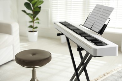 Photo of Synthesizer with music sheets and stool at home, closeup