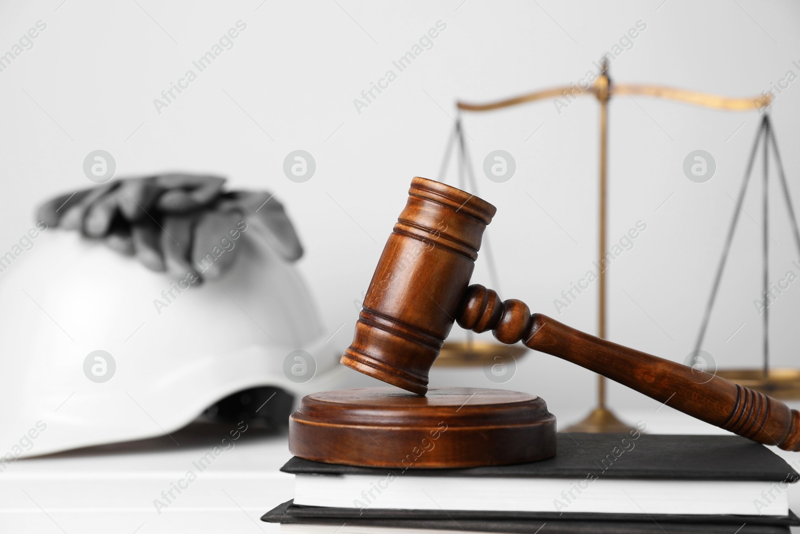 Photo of Accident at work concept. Gavel, scales and construction worker's protective gear on white wooden table, selective focus