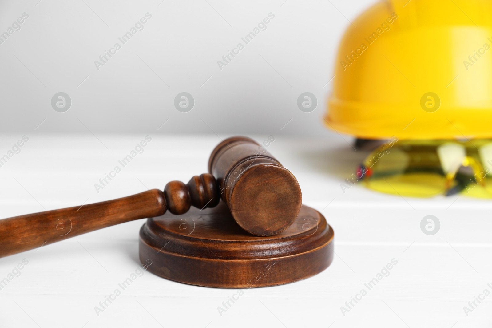 Photo of Accident at work concept. Gavel and construction worker's protective gear on white wooden table, selective focus