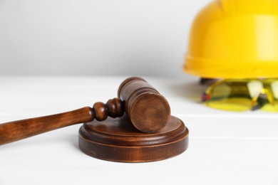 Photo of Accident at work concept. Gavel and construction worker's protective gear on white wooden table, selective focus