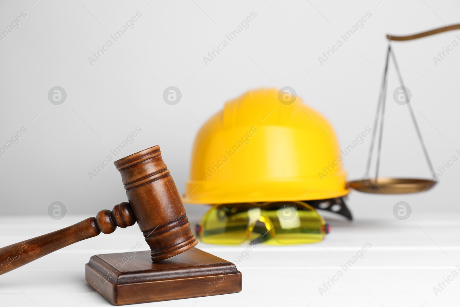 Photo of Accident at work concept. Gavel, scales and construction worker's protective gear on white wooden table, selective focus