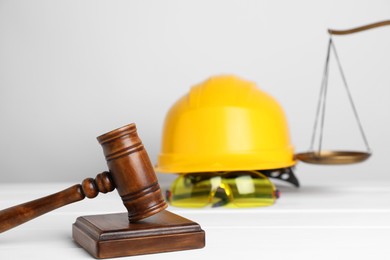 Photo of Accident at work concept. Gavel, scales and construction worker's protective gear on white wooden table, selective focus