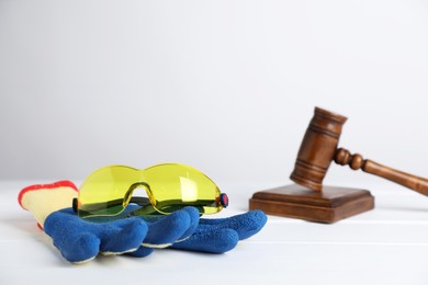 Photo of Accident at work concept. Gavel and construction worker's protective gear on white wooden table, selective focus