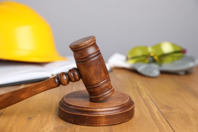 Photo of Accident at work concept. Gavel, book and construction worker's protective gear on wooden table, selective focus