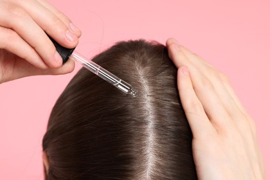 Photo of Hair loss problem. Girl applying serum onto hairline on pink background, closeup