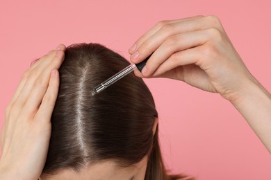 Photo of Hair loss problem. Girl applying serum onto hairline on pink background, closeup