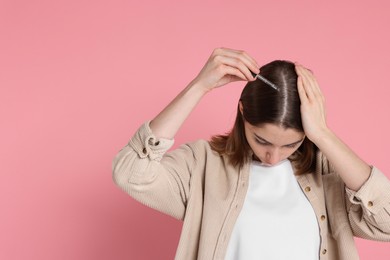 Photo of Hair loss problem. Girl applying serum onto hairline on pink background, space for text