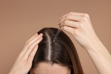 Photo of Hair loss problem. Girl applying serum onto hairline on dark beige background, closeup