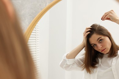 Photo of Hair loss problem. Girl applying serum onto hairline near mirror in bathroom