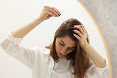 Photo of Hair loss problem. Girl applying serum onto hairline near mirror in bathroom