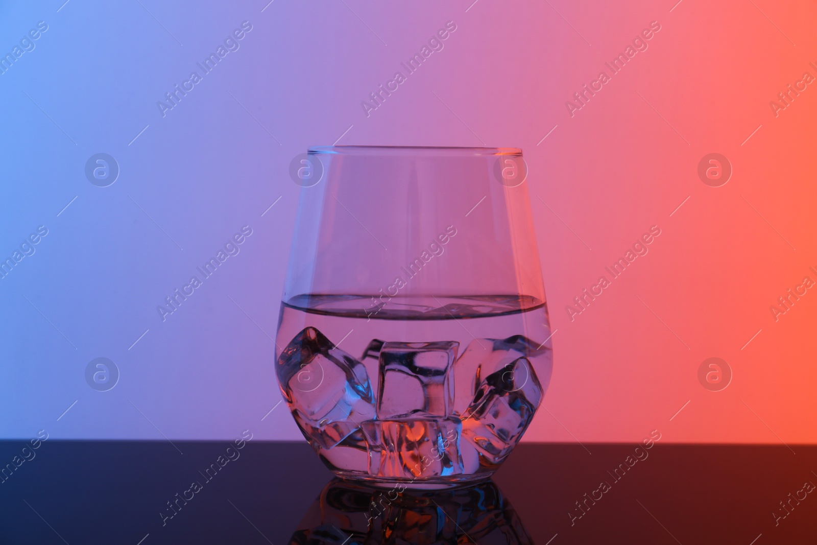 Photo of Glass with water and ice cubes on table against color background