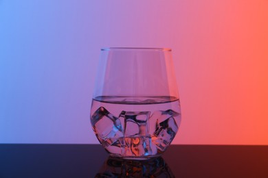 Photo of Glass with water and ice cubes on table against color background