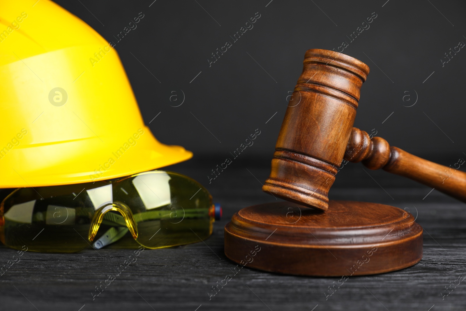 Photo of Accident at work concept. Gavel and construction worker's protective gear on black wooden table