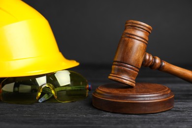 Photo of Accident at work concept. Gavel and construction worker's protective gear on black wooden table