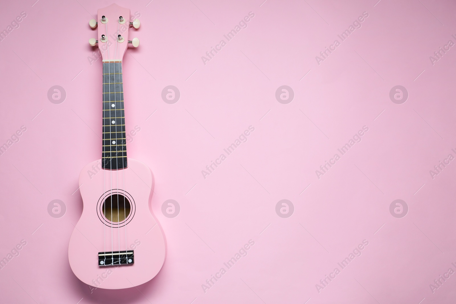 Photo of One ukulele on pink background, top view. Space for text