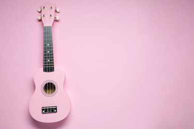 Photo of One ukulele on pink background, top view. Space for text