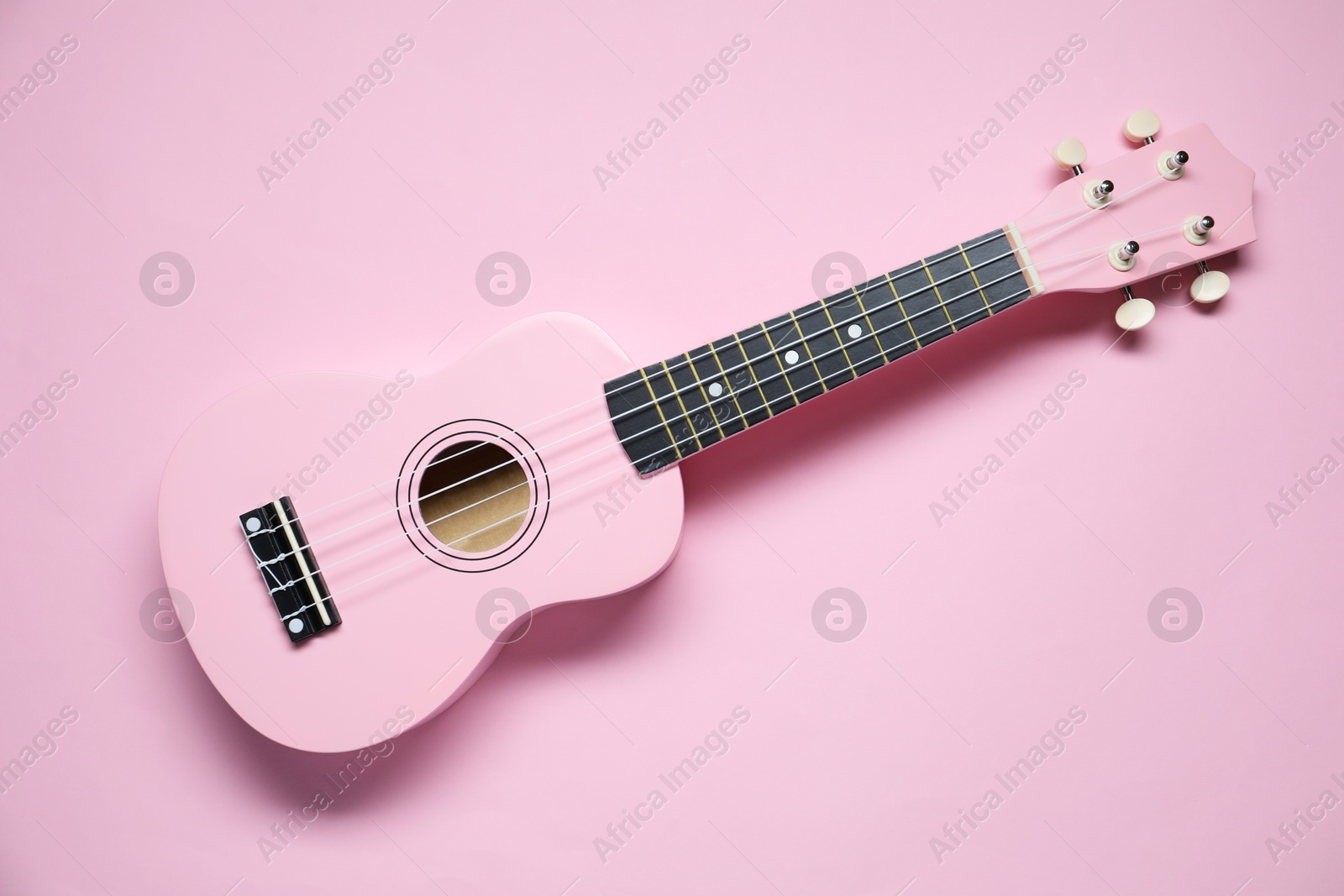 Photo of One ukulele on pink background, top view