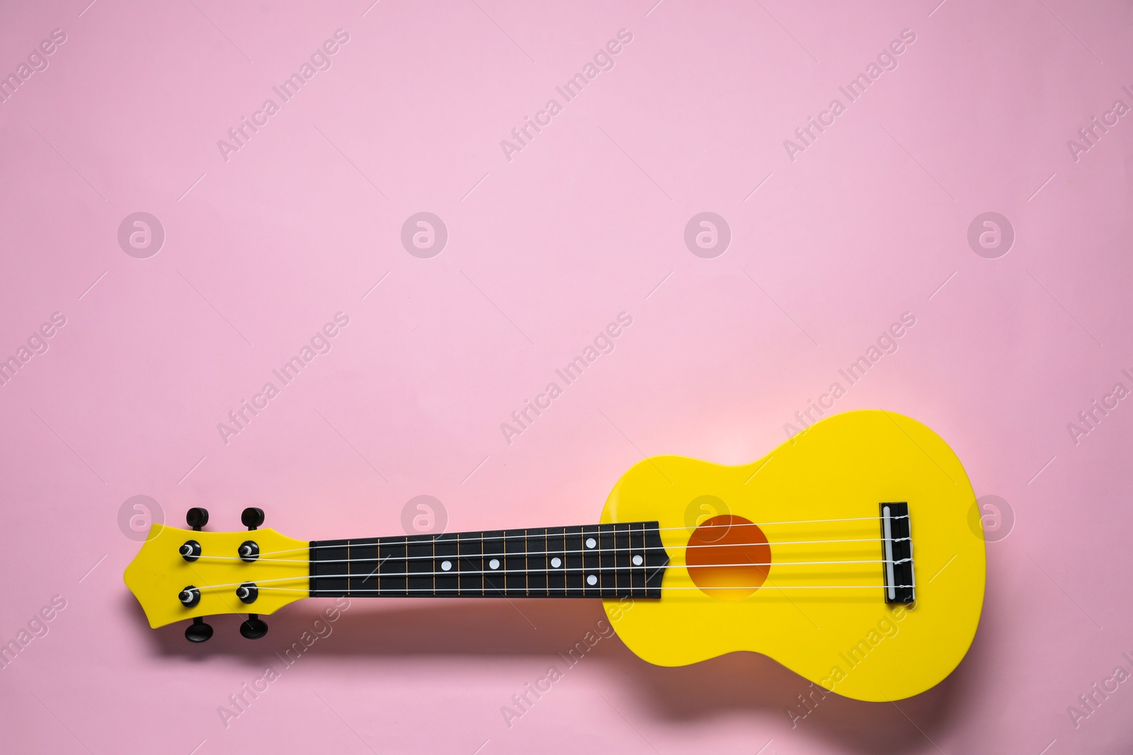 Photo of One ukulele on pink background, top view. Space for text