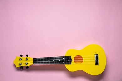 Photo of One ukulele on pink background, top view. Space for text