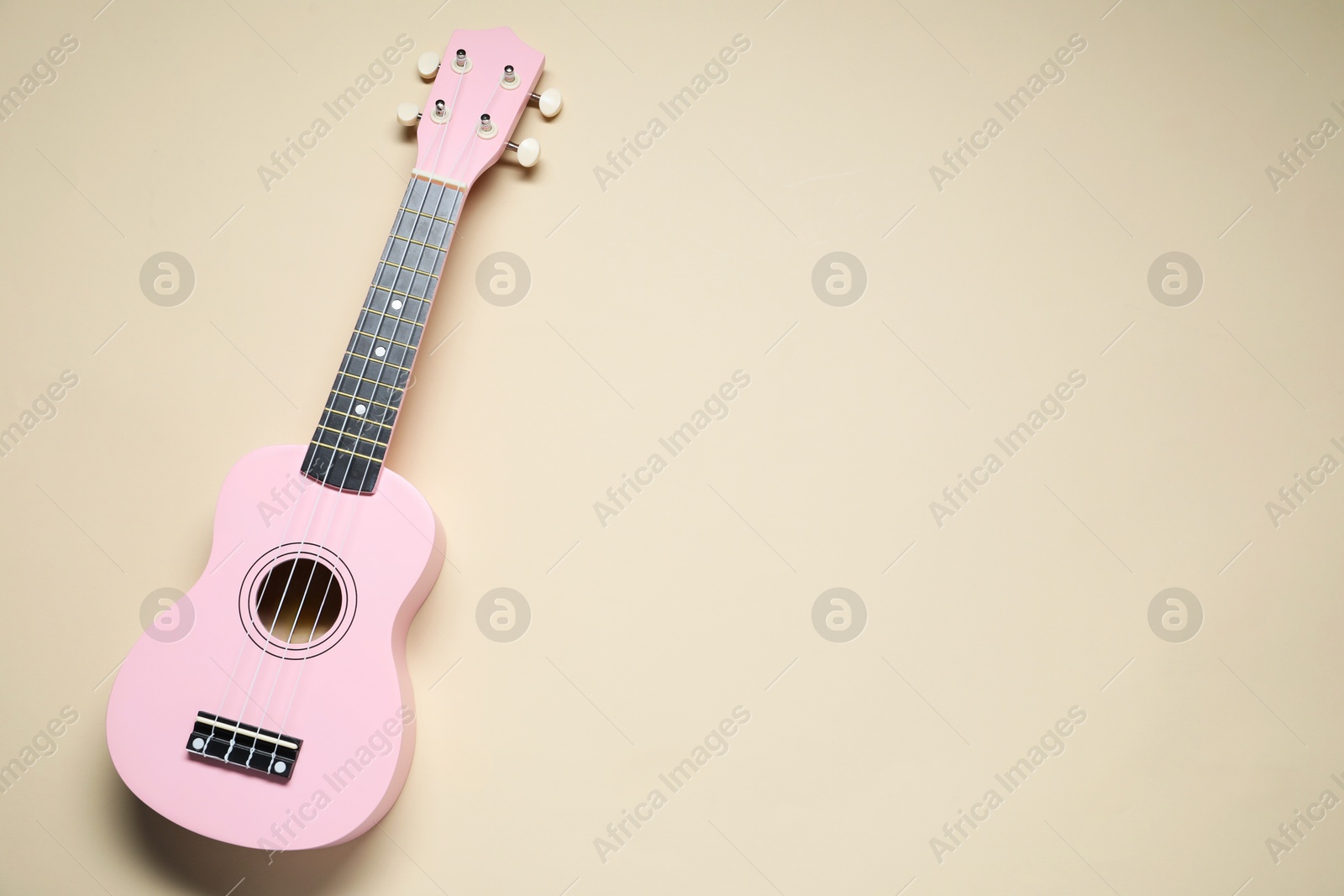 Photo of One ukulele on beige background, top view. Space for text