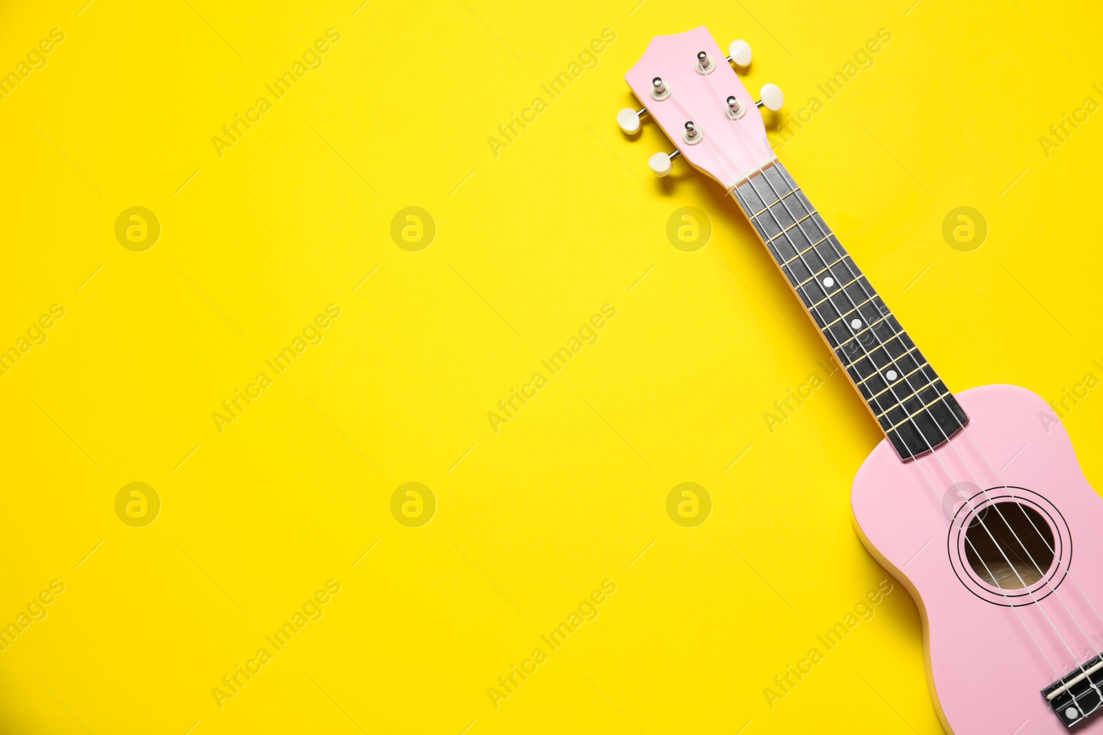 Photo of One ukulele on yellow background, top view. Space for text