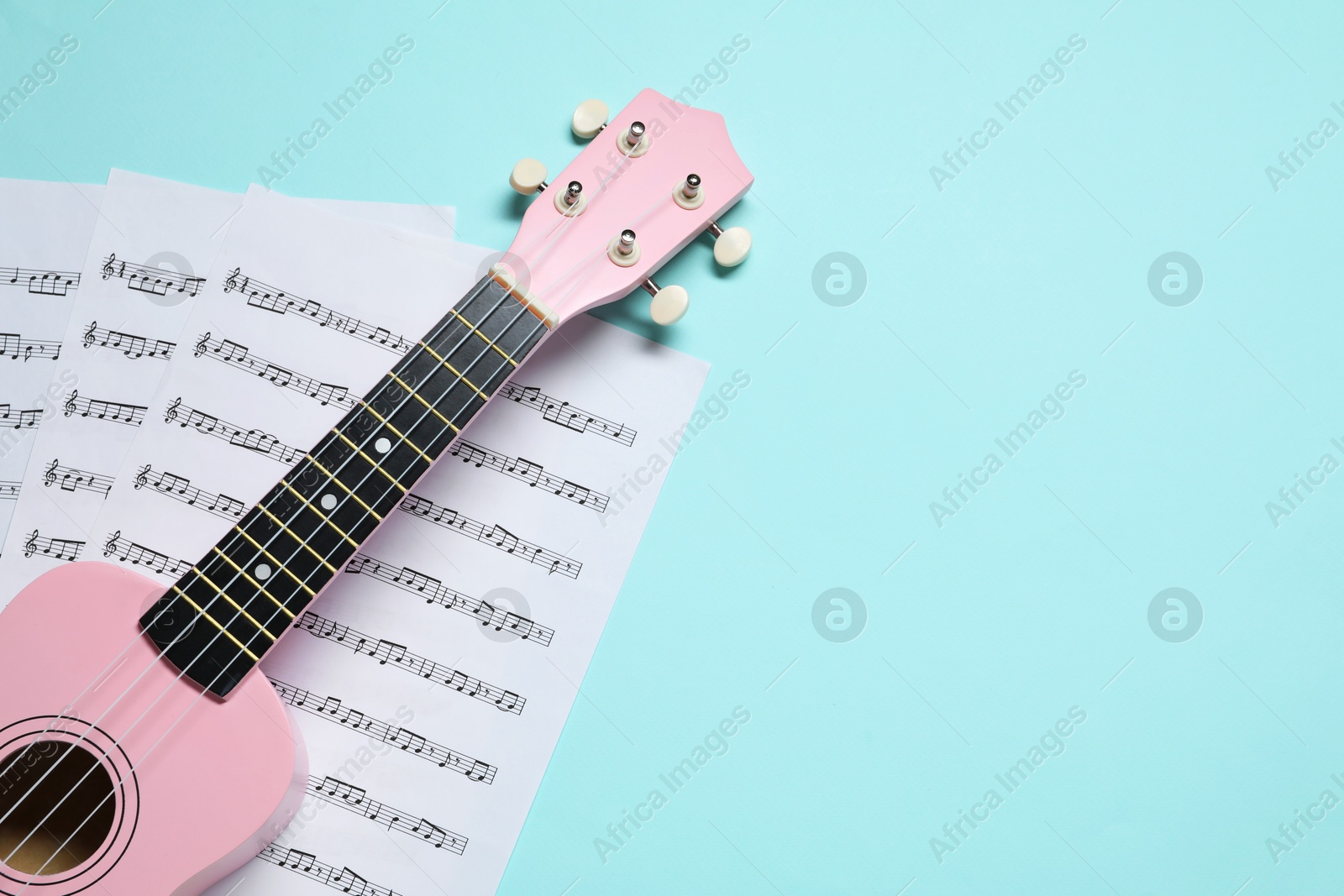 Photo of Ukulele and music sheets on light blue background, top view. Space for text