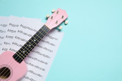 Photo of Ukulele and music sheets on light blue background, top view. Space for text