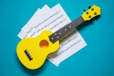 Ukulele and music sheets on light blue background, top view