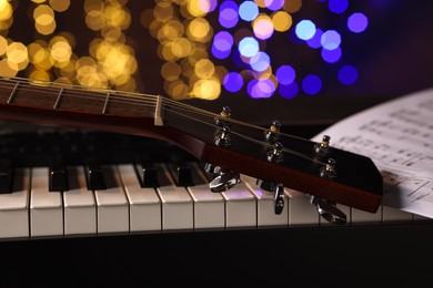 Photo of Guitar and notes on piano against blurred lights, closeup. Bokeh effect