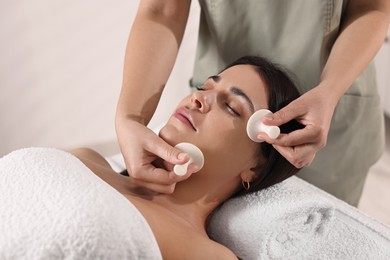 Photo of Young woman receiving facial massage with spa stones in salon