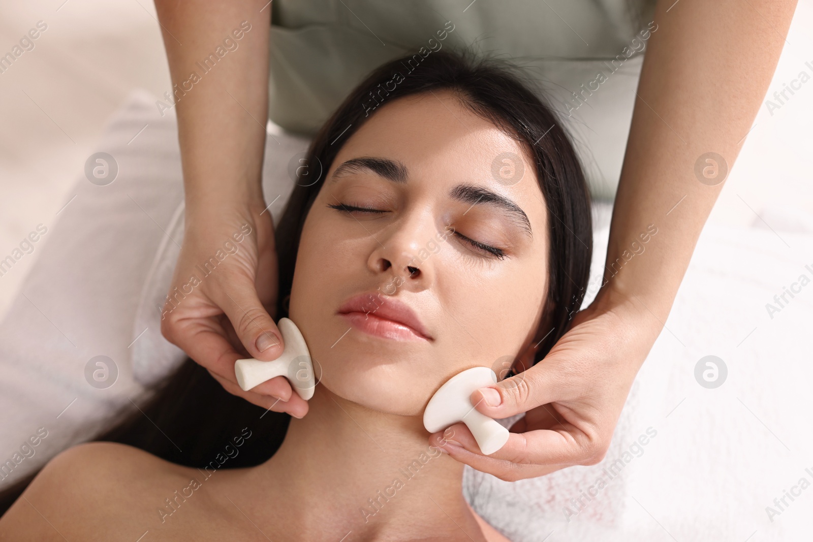 Photo of Young woman receiving facial massage with spa stones in salon