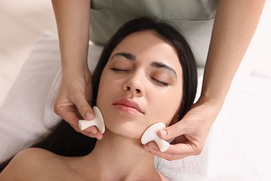 Photo of Young woman receiving facial massage with spa stones in salon