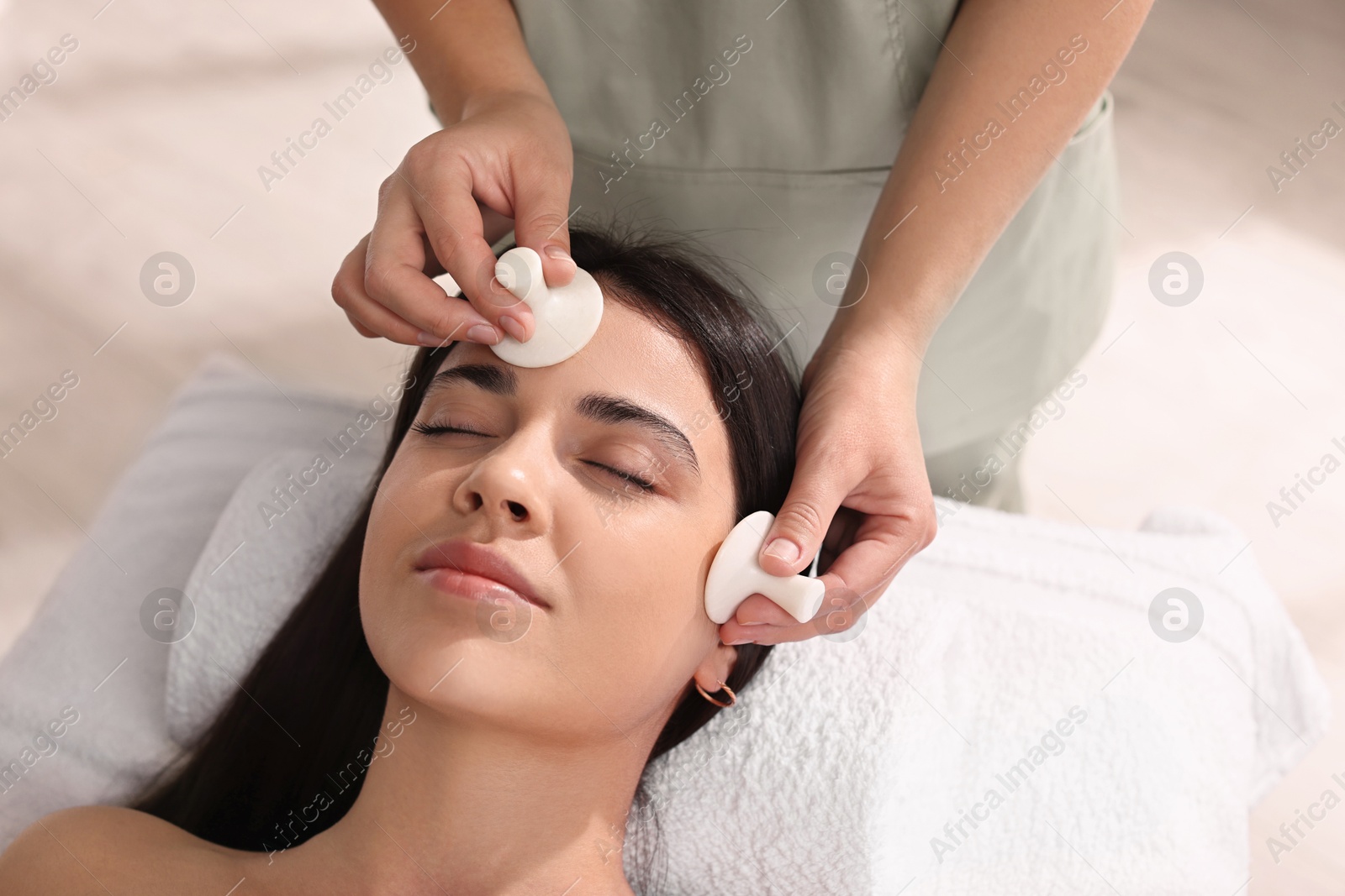 Photo of Young woman receiving facial massage with spa stones in salon