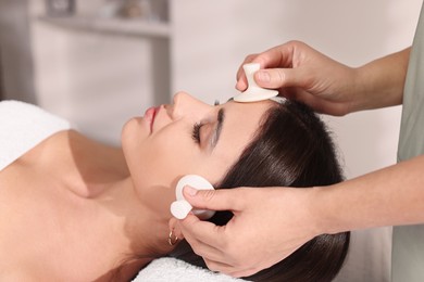 Photo of Young woman receiving facial massage with spa stones in salon