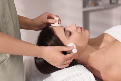 Photo of Young woman receiving facial massage with spa stones in salon