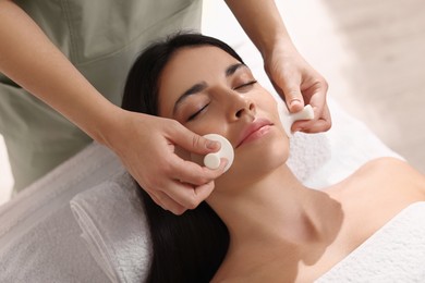 Photo of Young woman receiving facial massage with spa stones in salon