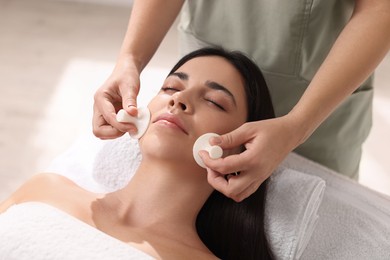 Photo of Young woman receiving facial massage with spa stones in salon