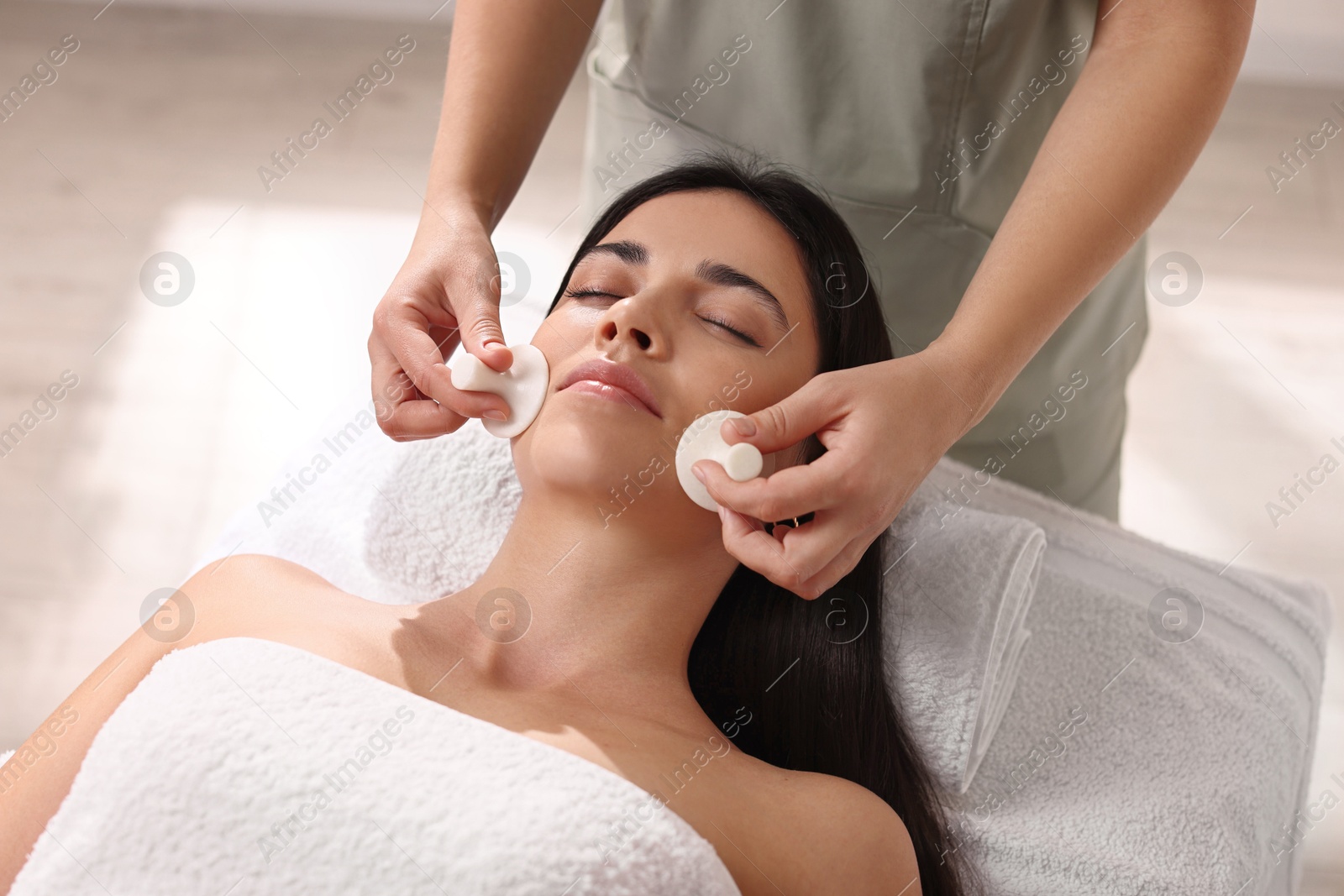 Photo of Young woman receiving facial massage with spa stones in salon