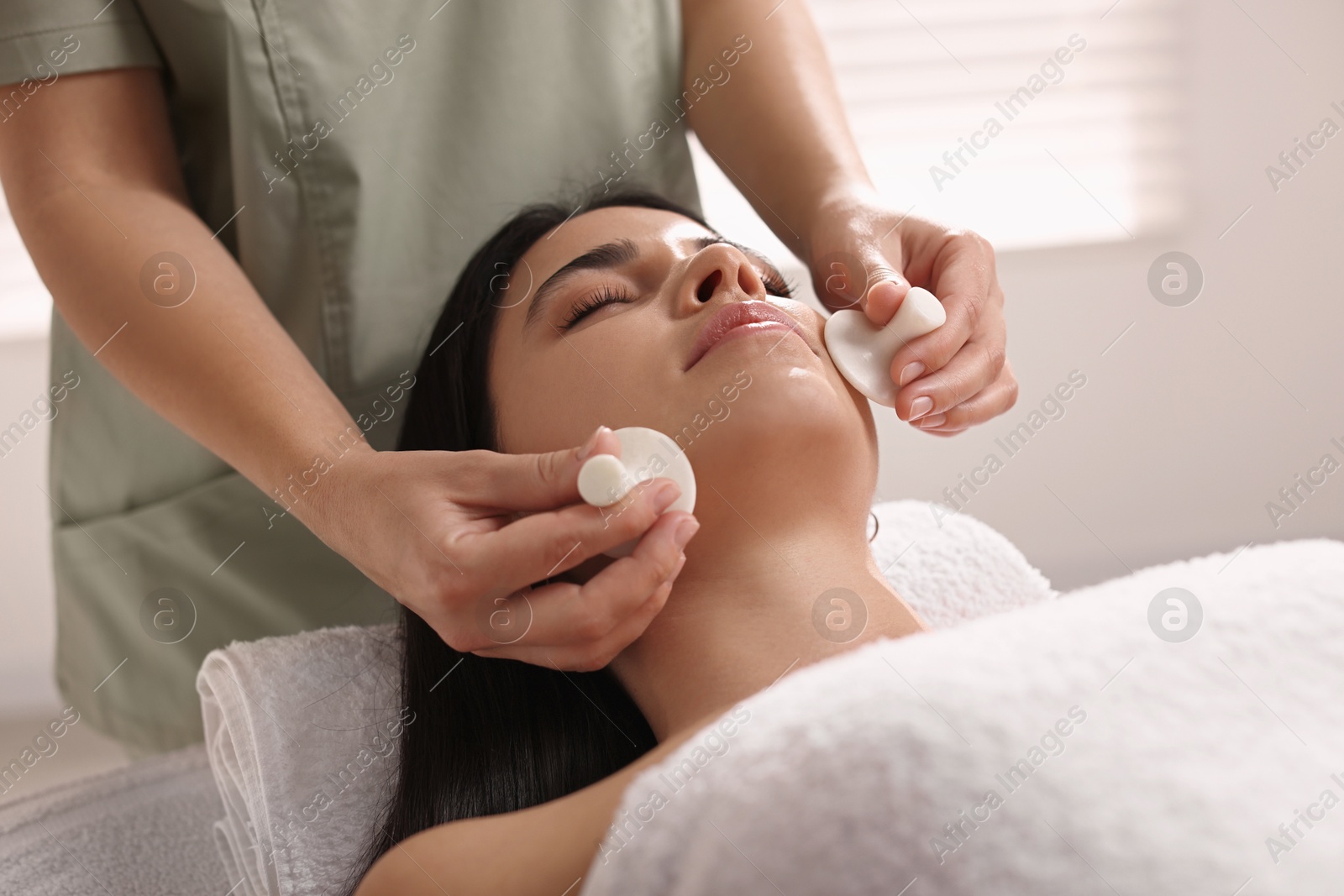 Photo of Young woman receiving facial massage with spa stones in salon