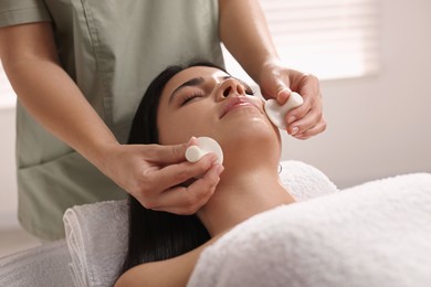 Photo of Young woman receiving facial massage with spa stones in salon