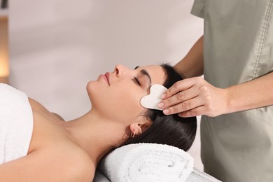 Photo of Young woman receiving facial massage with gua sha tool in spa salon