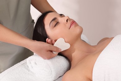 Photo of Young woman receiving facial massage with gua sha tool in spa salon