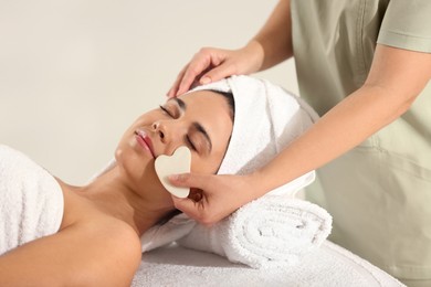 Photo of Young woman receiving facial massage with gua sha tool in spa salon