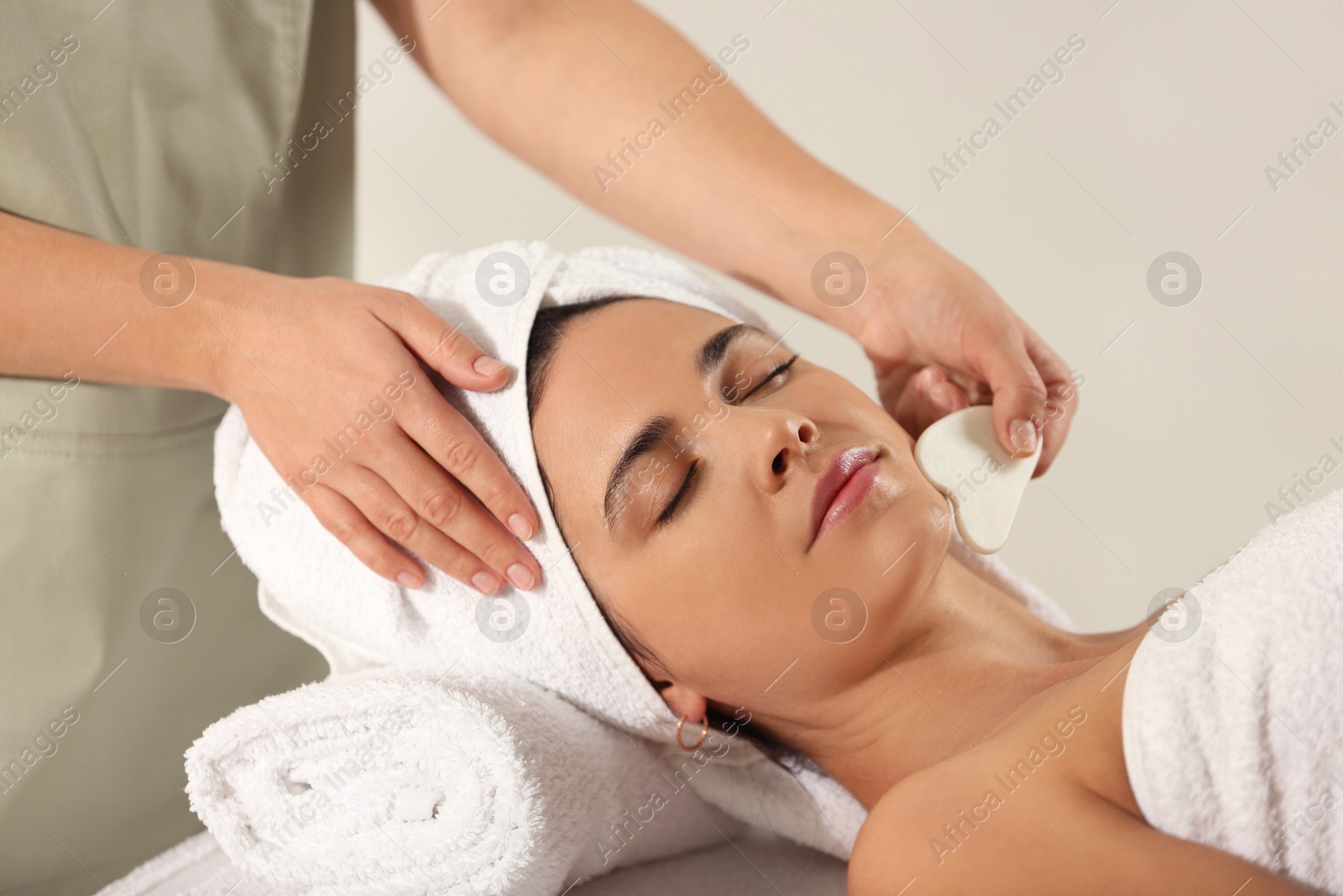 Photo of Young woman receiving facial massage with gua sha tool in spa salon