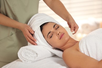 Photo of Young woman receiving facial massage with gua sha tool in spa salon