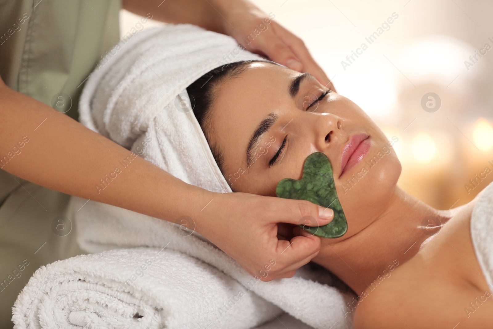 Photo of Young woman receiving facial massage with gua sha tool in spa salon