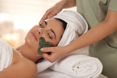 Photo of Young woman receiving facial massage with gua sha tool in spa salon