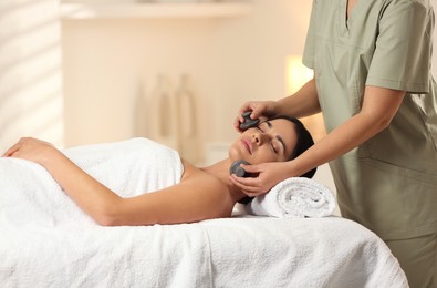 Photo of Young woman receiving facial massage with spa stones in salon