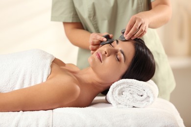 Photo of Young woman receiving facial massage with spa stones in salon